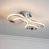 Endon Neve semi-flush ceiling light with swirling looped LED bands in polished chrome, mounted to a ceiling above white cornice.