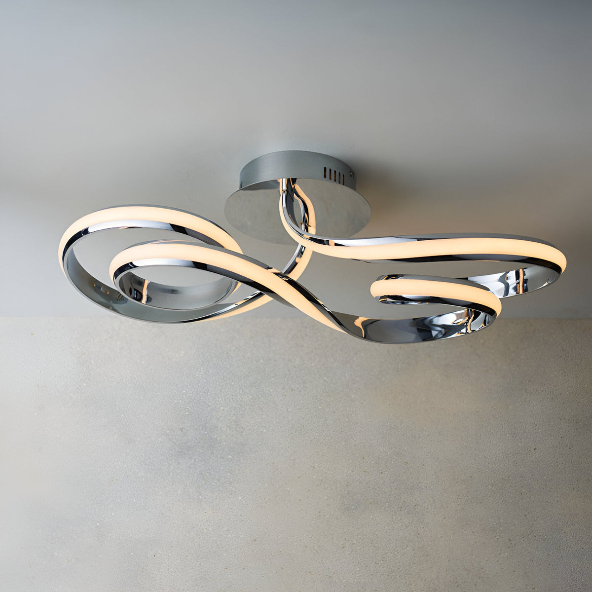 Endon Neve LED semi-flush ceiling light with swirling looped arms in polished chrome, mounted to a neutral ceiling above a light wall.