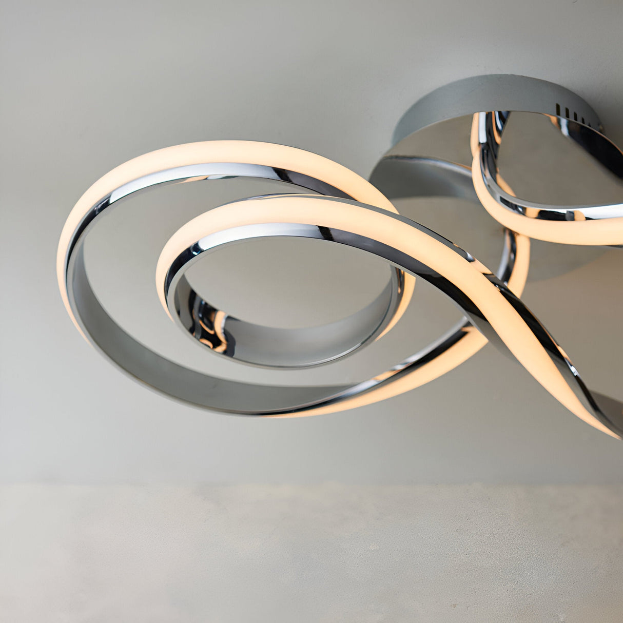 Endon Neve semi-flush ceiling light in polished chrome, shown close-up with interlocking looped LED bands mounted to a light ceiling.