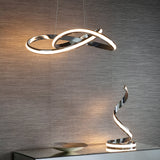 Endon Neve chrome LED pendant light with looping sculptural curves and white diffuser, shown lit above a matching spiral table lamp on a grey textured wall.