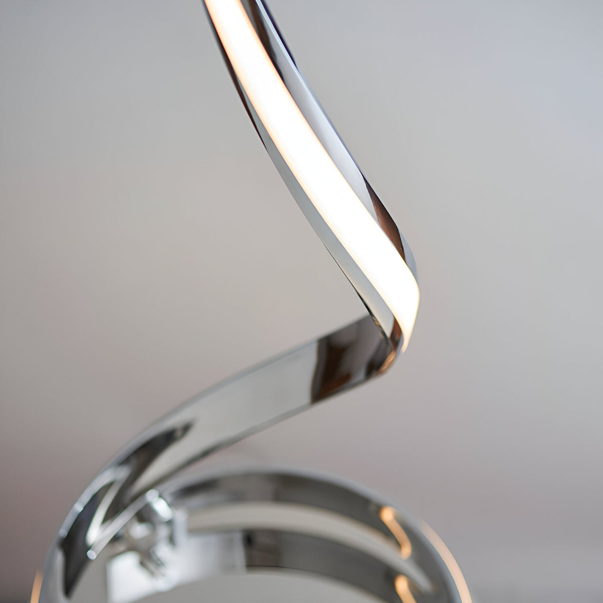 Close-up of the Neve Floor Lamp's spiralling chrome curve with a warm white LED diffuser, set against a plain light grey background.