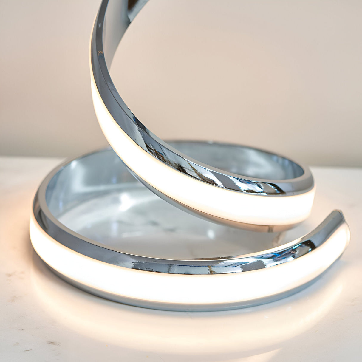 Close-up of the Endon Neve table lamp base showing polished chrome curves with an integrated LED white diffuser coiled on a light surface.