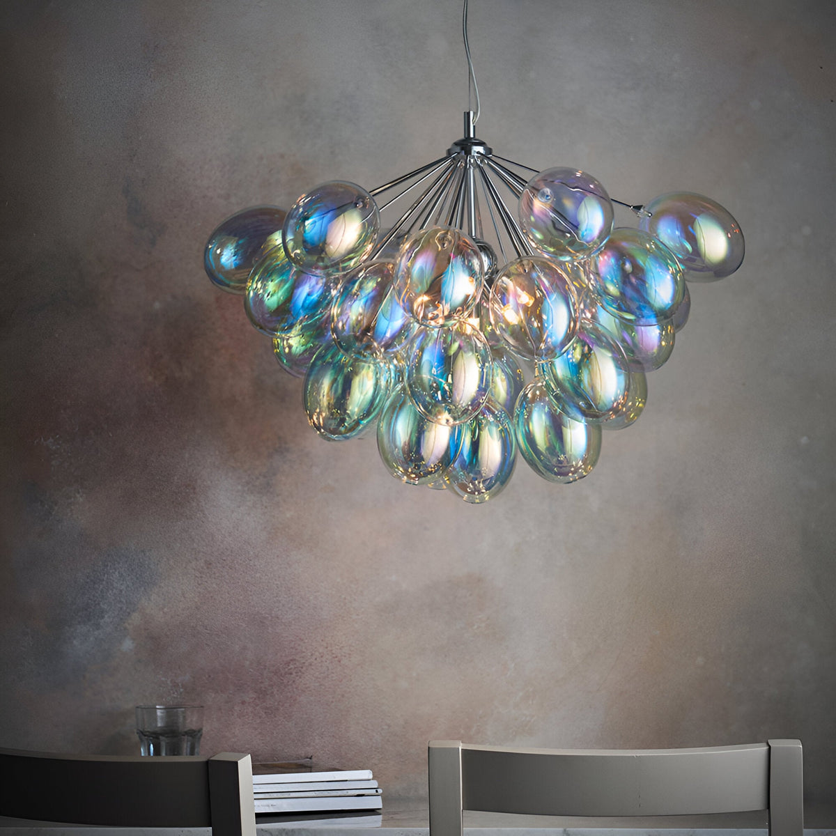Endon Brenworth 6 light pendant in chrome with clustered iridescent glass shades, suspended above a dining setting against a textured grey wall.