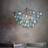 Endon Brenworth 6 light pendant in chrome with clustered iridescent glass shades, suspended above a dining setting against a textured grey wall.
