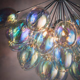 Close-up of Endon Brenworth 6 Light Pendant showing clustered iridescent glass shades in blue, green and amber tones suspended from chrome rods.