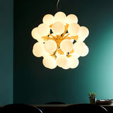 Fitzroy 28 Light Pendant in brushed brass with clustered white opal glass globes, hung above a dining table against a dark teal wall.
