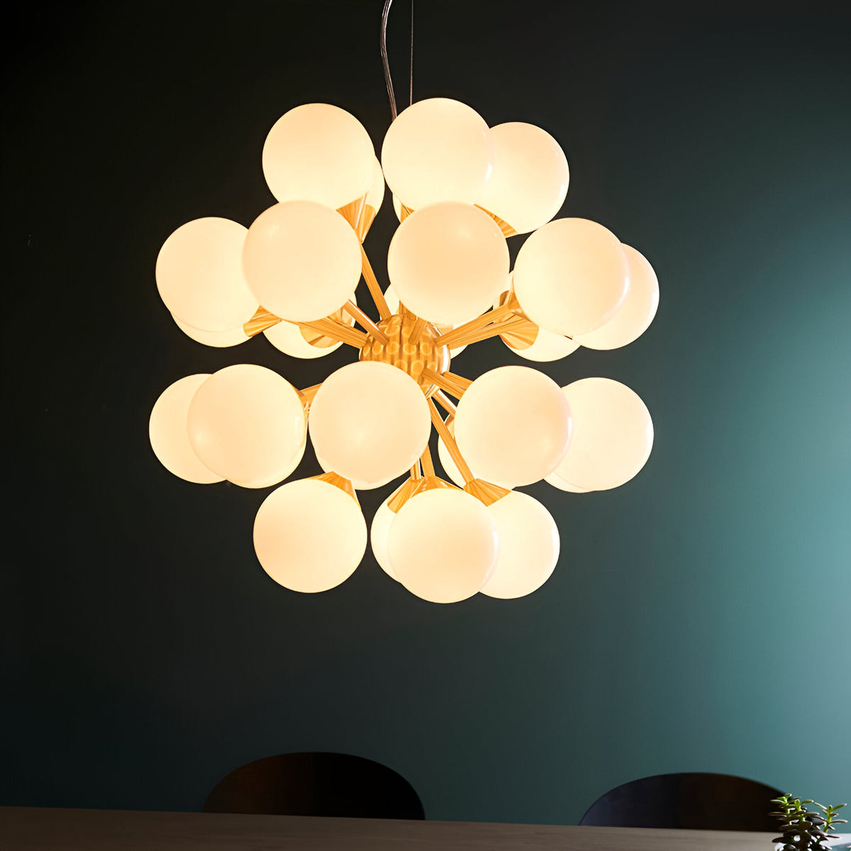 Fitzroy 28 Light Pendant in brushed brass with clustered white opal glass globe shades, hung above a dining table against a dark teal wall.