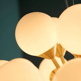 Fitzroy 28 Light Pendant close-up showing round opal glass globe shades on brushed brass fittings against a dark teal background.