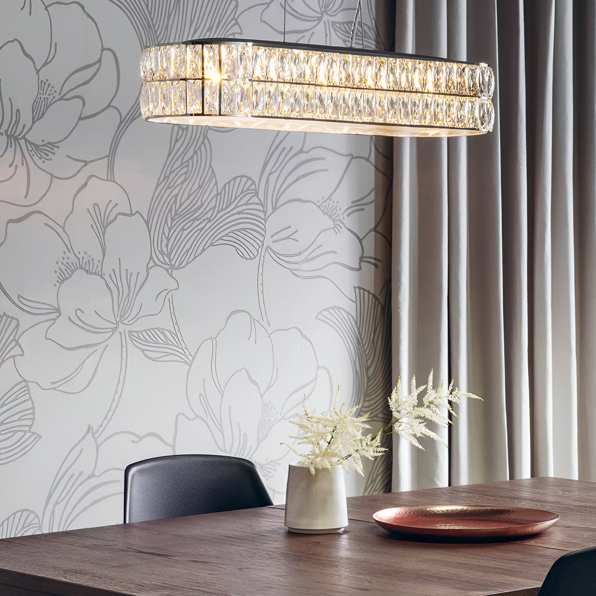 Endon Marguerite linear pendant in polished chrome with faceted crystals, illuminated above a wooden dining table against a floral wallpaper backdrop.