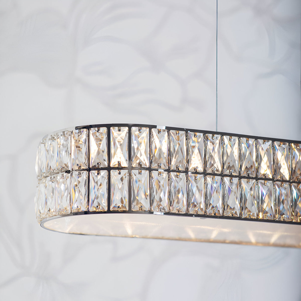 Endon Marguerite linear pendant in polished chrome with two rows of faceted crystals and a prismatic glass diffuser, shown lit against a light wall.