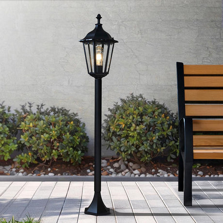 Endon Ashshaw traditional bollard light in matt black die cast aluminium with a lantern head, clear glass panels and filament E27 bulb, set on a patio.