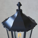 Close-up of the Endon Ashshaw bollard light in matt black die cast aluminium, showing the lantern top, decorative finial and filament bulb behind clear glass.