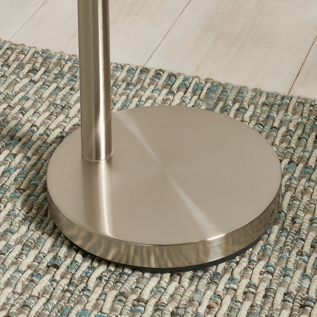 Close-up of the Endon Brockcombe floor lamp's round satin nickel base and stem on a woven blue and grey rug over pale wood flooring.
