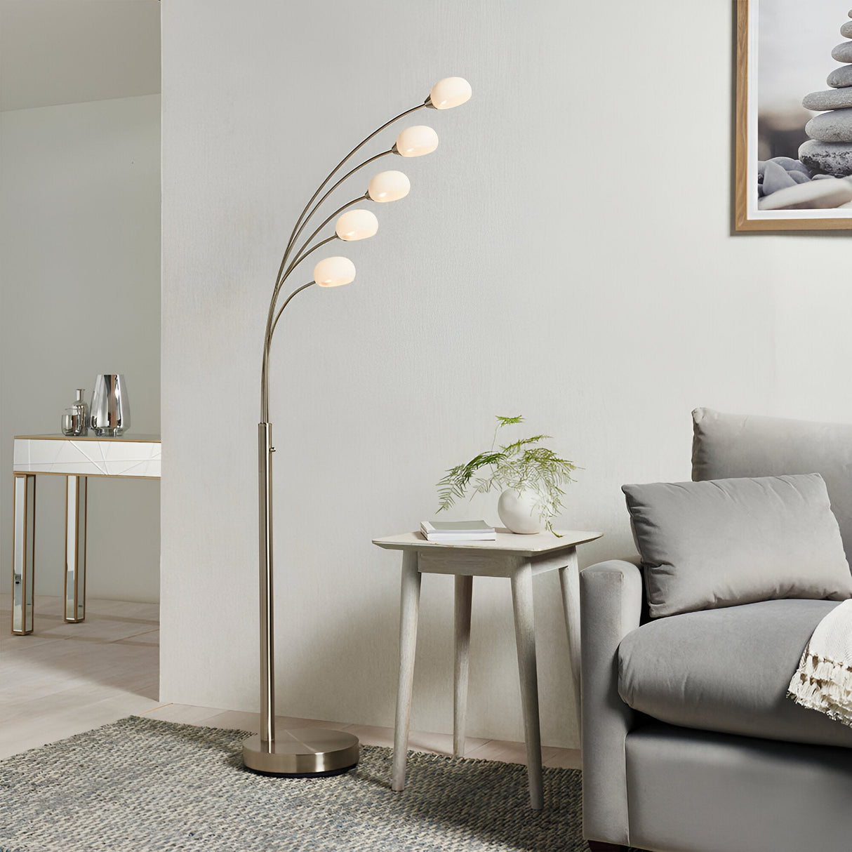 Brockcombe 5 Light Floor Lamp in satin nickel with arched arms and white glass shades, shown beside a grey sofa and side table in a living room.