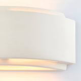 Close-up of the Endon Bramhurst white ceramic wall light showing its curved matt form casting a warm up-and-down glow against a plain wall.