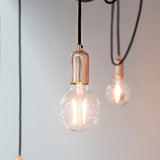 Endon Marlowe 6 Light Pendant in copper and black with exposed filament bulbs on black fabric cables against a pale grey wall.