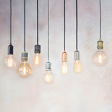 Endon Marlowe pendant lights in black, copper, chrome, brass and concrete finishes hanging with exposed filament bulbs against a neutral wall.