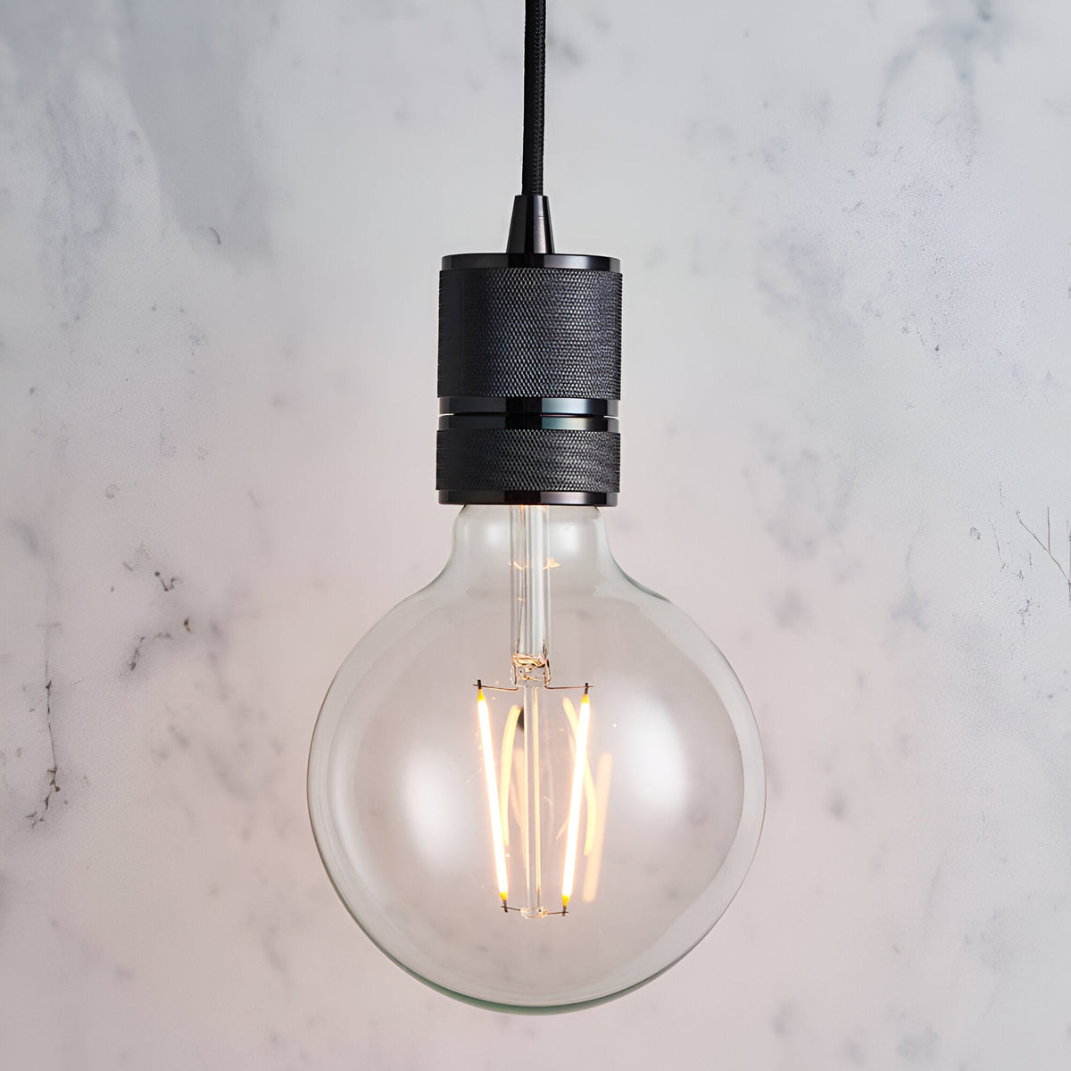 Endon Camden pendant light with a black chrome knurled lamp holder on a black fabric flex, fitted with a clear E27 globe filament bulb against marble.