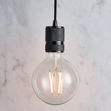 Endon Camden pendant light with a black chrome knurled lamp holder on a black fabric flex, fitted with a clear E27 globe filament bulb against marble.