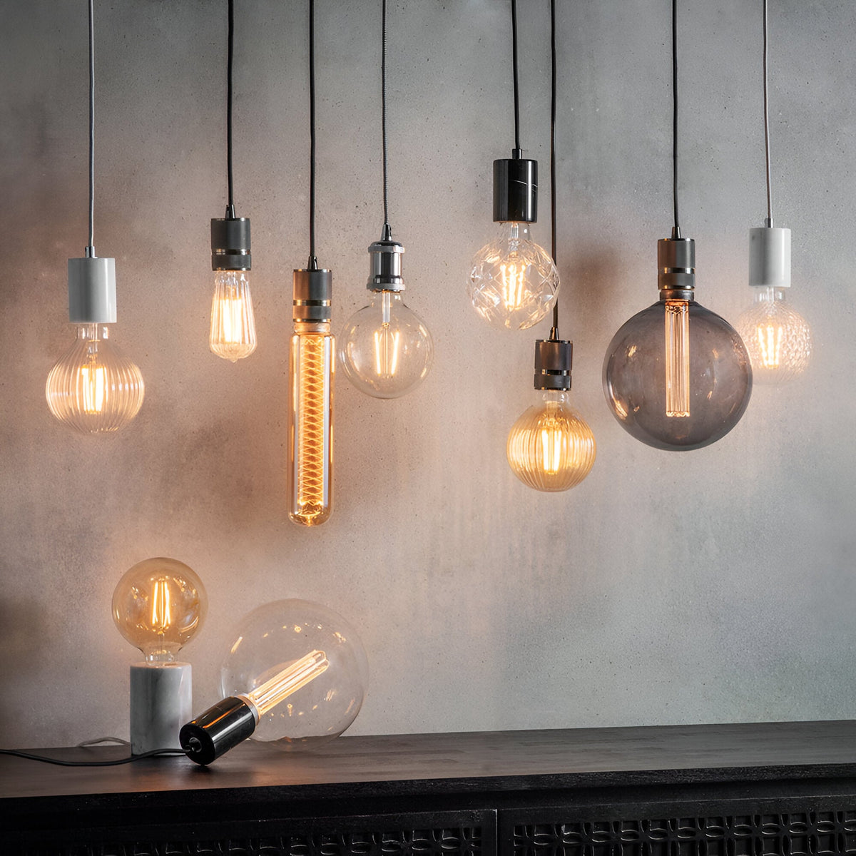 Endon Camden pendant lights in chrome and black hung in a cluster with exposed filament and smoked glass bulbs against a grey concrete wall.