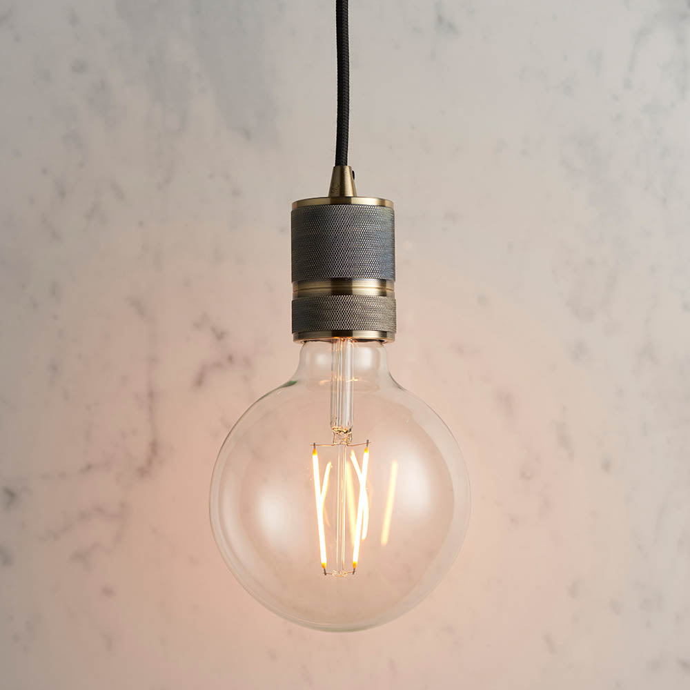 Endon Camden pendant light with antique brass knurled holder, black fabric flex and exposed E27 filament globe bulb against a light marble background.