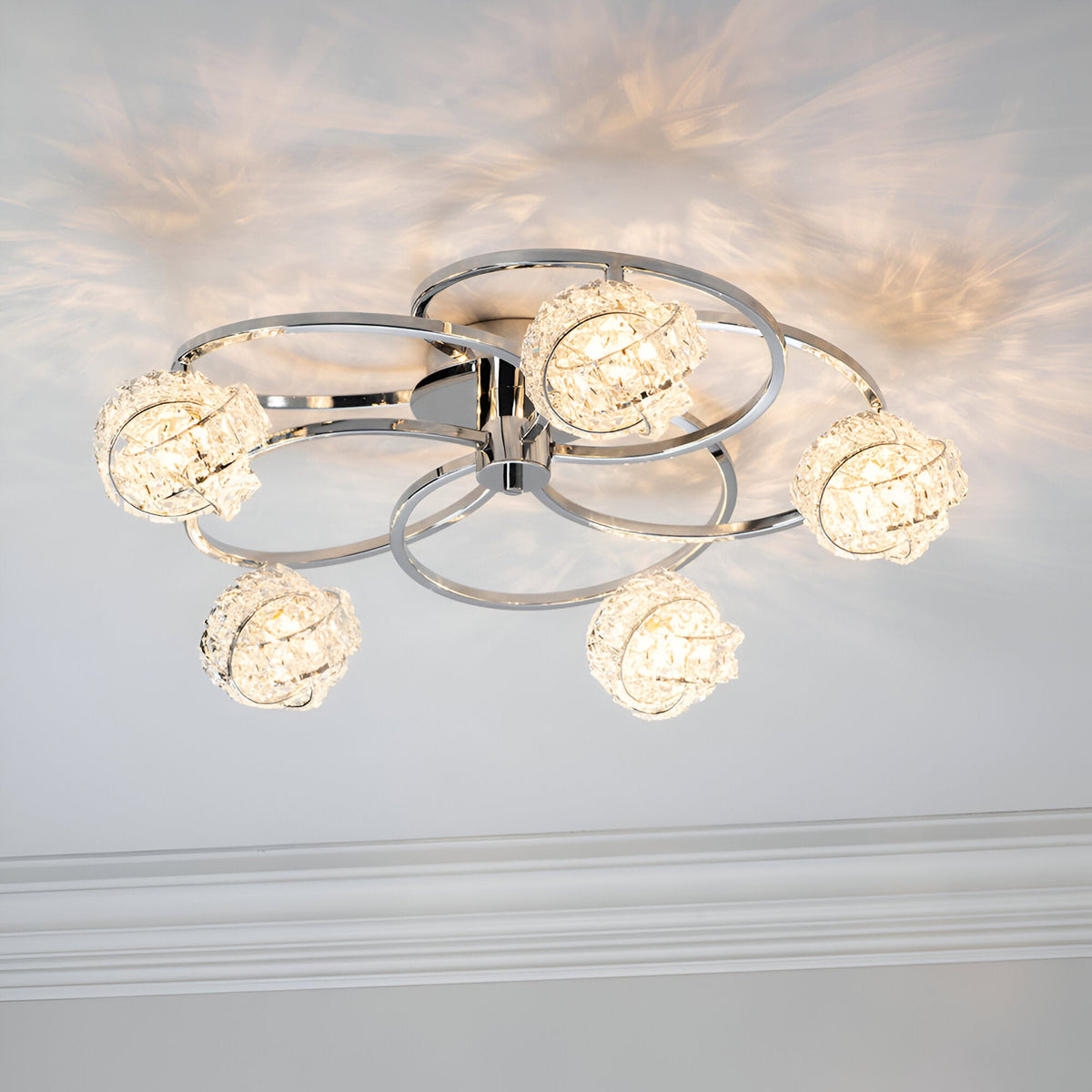Endon Seraphine 5 light semi-flush ceiling light in polished chrome, illuminated crystal globe shades on circular arms casting patterns across the ceiling.