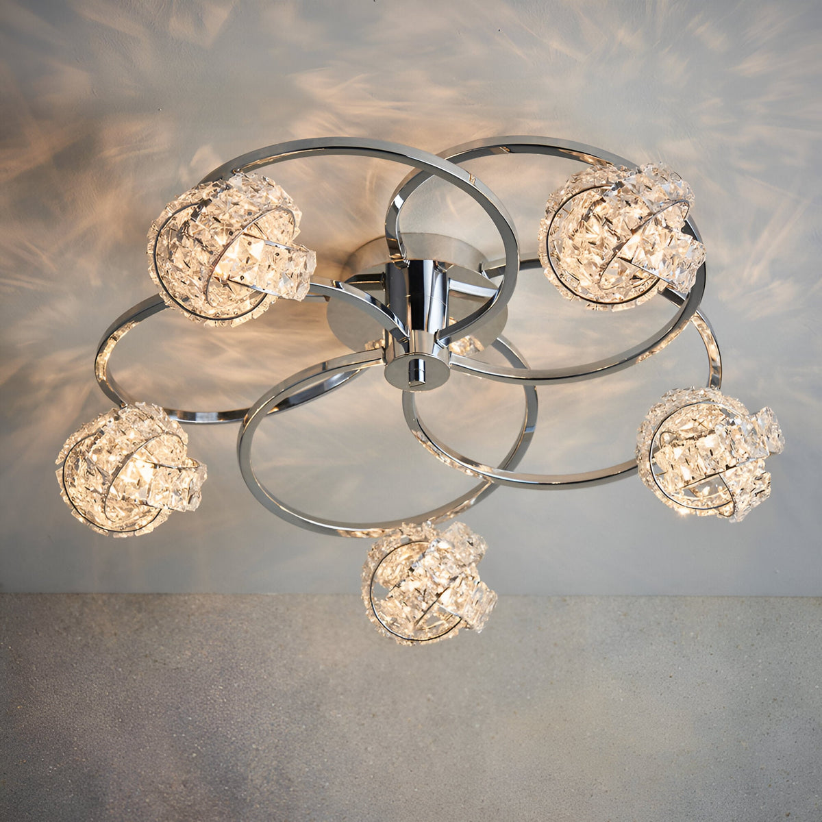 Endon Seraphine 5 light semi-flush ceiling light with polished chrome rings and crystal globe shades, shown lit against a pale wall.