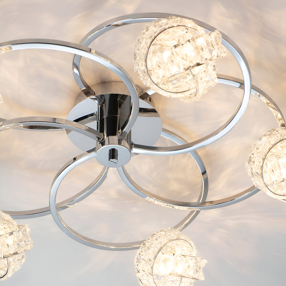 Endon Seraphine 5 light semi-flush ceiling light in polished chrome, with looped ring arms and crystal glass shades, viewed close-up from below.