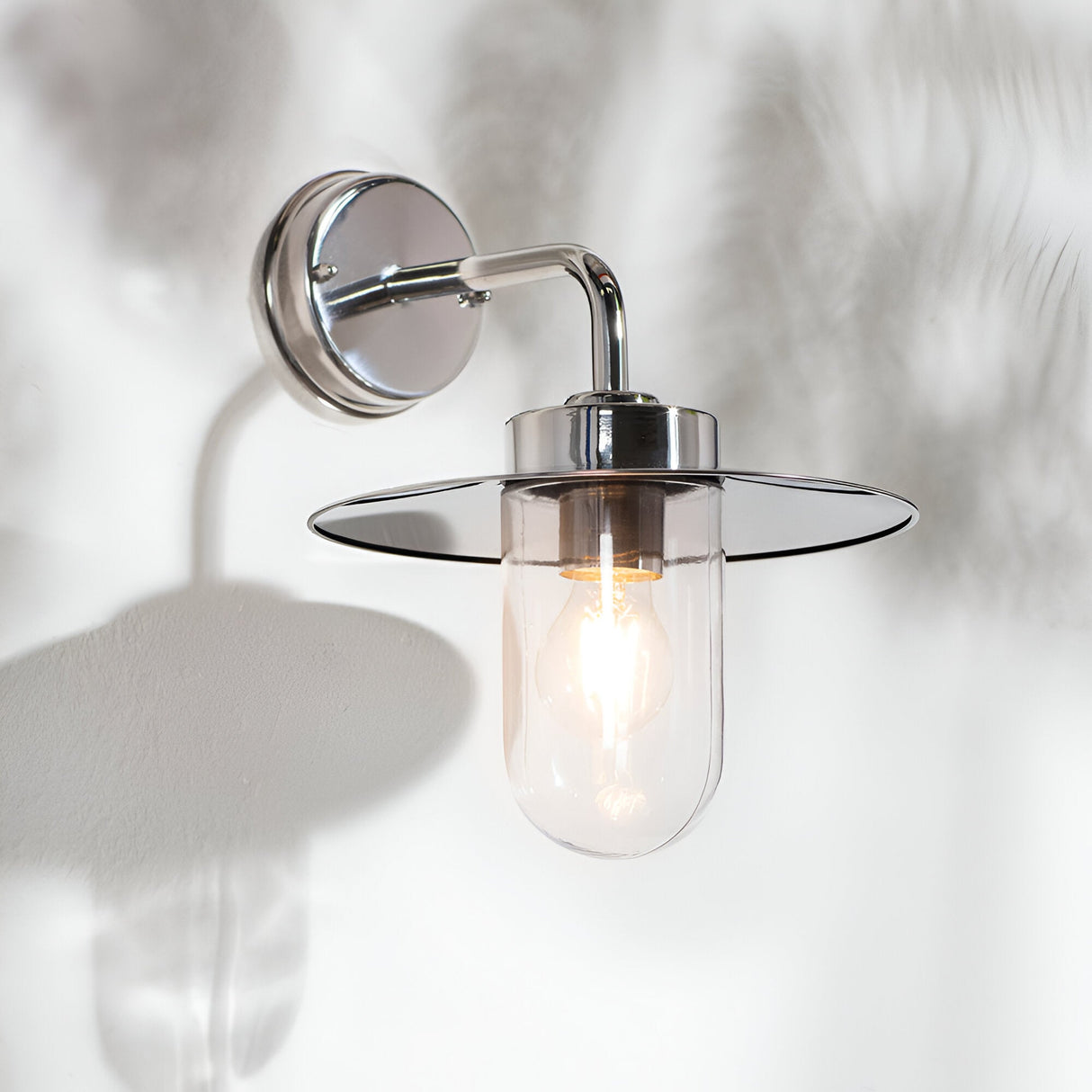 Endon Aldbury outdoor wall light in polished stainless steel with a clear glass shade and E27 filament bulb, mounted on a pale wall.