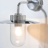 Endon Aldbury outdoor wall light in polished stainless steel with a clear glass shade and lit E27 filament bulb, mounted on a white wall.