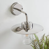 Endon Aldbury outdoor wall light in polished stainless steel with a domed disc shade and clear glass lantern shade, mounted on a white wall beside a fern.