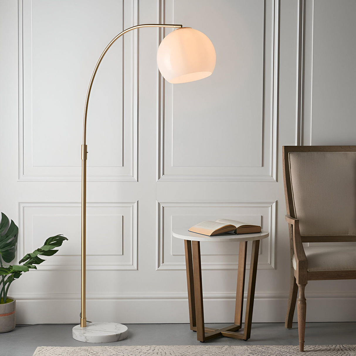Endon Sinclair arc floor lamp with brushed brass stem, gloss white glass globe shade and polished white marble base, beside a side table and chair.