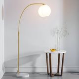 Endon Sinclair floor lamp with arched brass stem, gloss white glass globe shade and marble base, beside a round side table in a light interior.