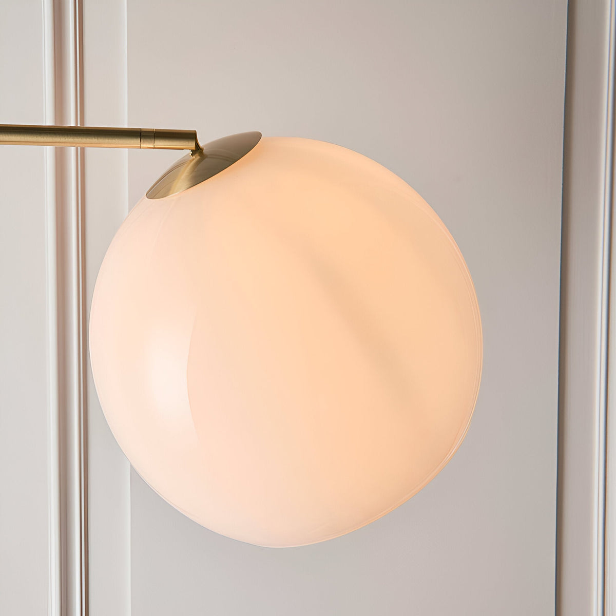 Close-up of the Endon Sinclair floor lamp's gloss white glass globe shade with brushed brass fitting, set against a pale panelled wall.