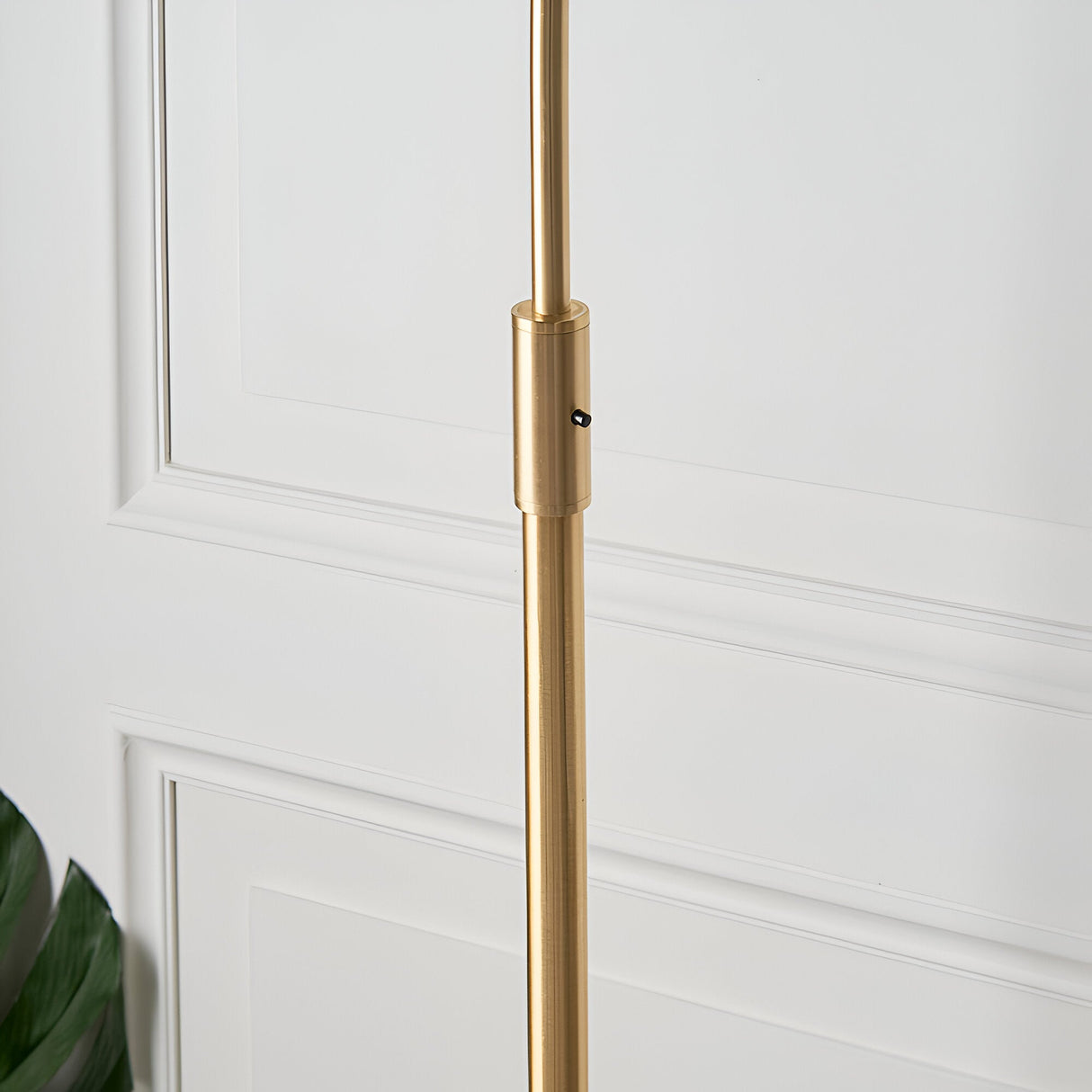 Close-up of the Endon Sinclair floor lamp's brushed brass stem with adjustment collar and switch, set against a white panelled wall.