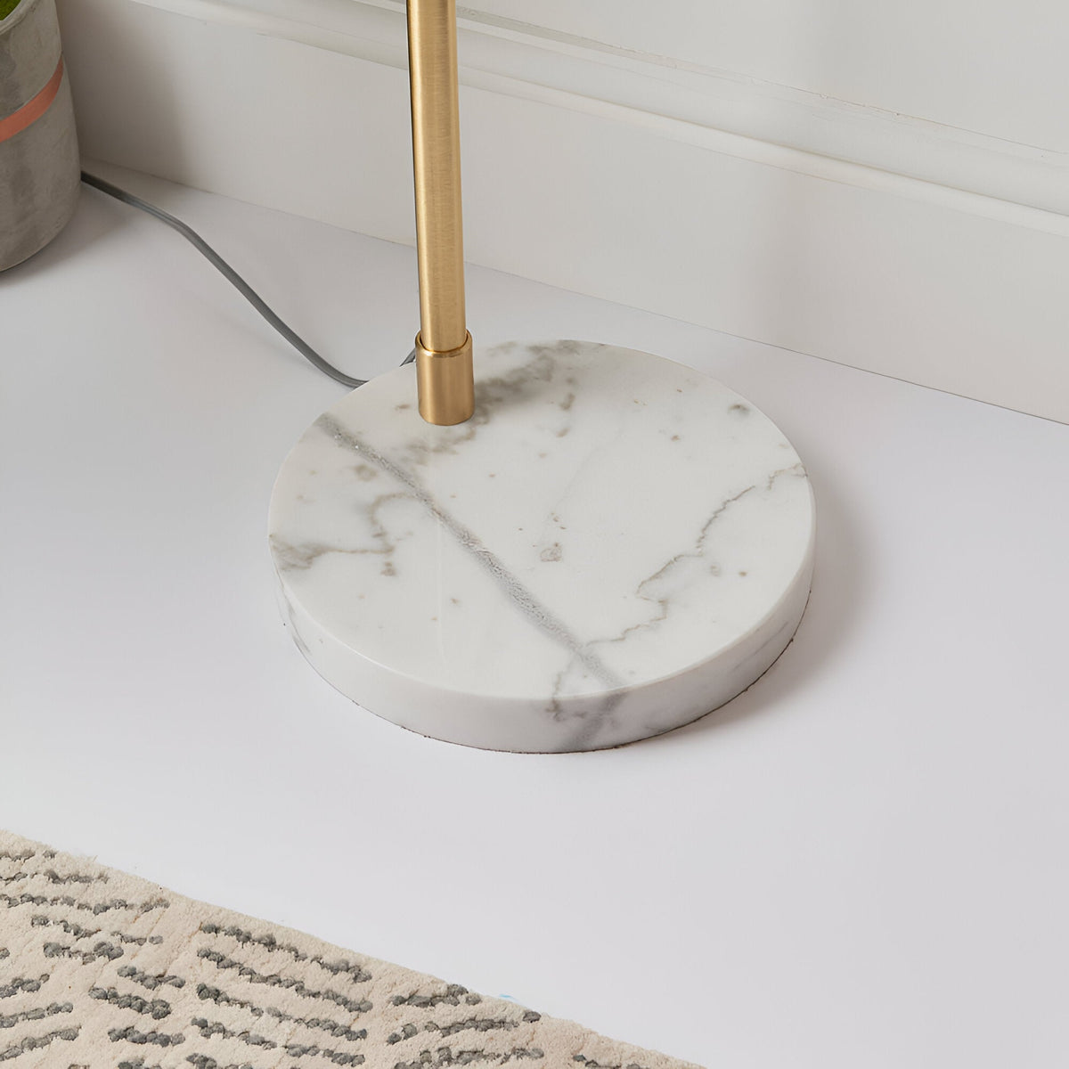 Close-up of the Endon Sinclair floor lamp's polished white and grey marble base with a slender brushed brass stem, shown on a light floor beside a rug.
