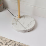 Close-up of the Endon Sinclair floor lamp's polished white and grey marble base with a slender brushed brass stem, shown on a light floor beside a rug.