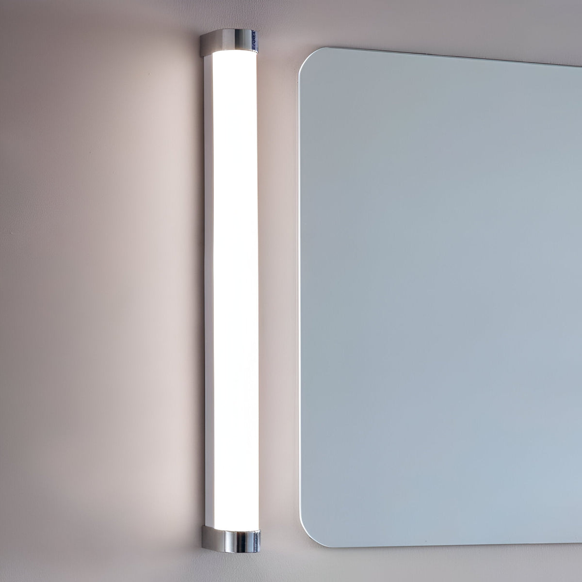 Endon Carlshaw LED large bathroom wall light mounted vertically beside a rounded rectangular mirror, with a slim white ribbed diffuser and chrome end caps.
