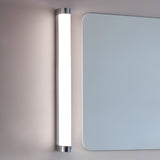 Endon Carlshaw LED large bathroom wall light mounted vertically beside a rounded rectangular mirror, with a slim white ribbed diffuser and chrome end caps.