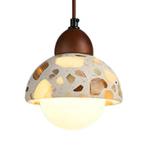 The Terroso 1 Light Dome Travertine Single Pendant Light features a round white bulb with a dome-shaped light beige travertine shade, earthy stone patterns, and is suspended by a walnut brown cord and fixture.