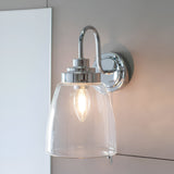 Endon Aldhurst chrome bathroom wall light with clear glass dome shade, curved arm and round backplate, mounted beside a mirror with lit E14 bulb.