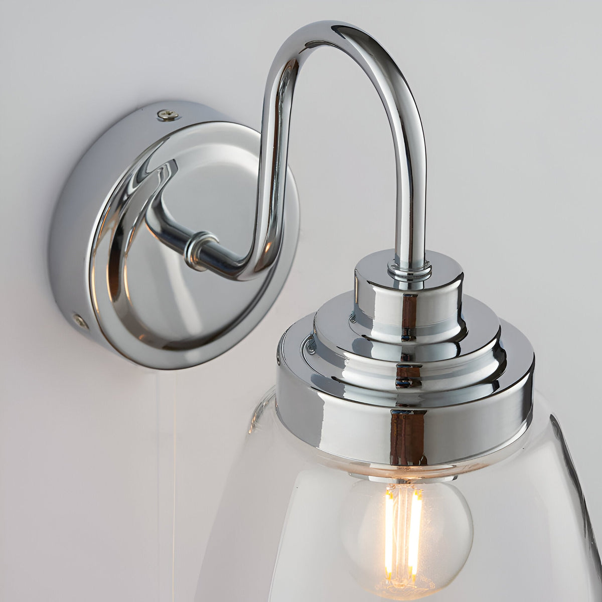 Endon Aldhurst bathroom wall light close-up showing polished chrome backplate, curved arm, and clear glass shade with an E14 filament bulb.
