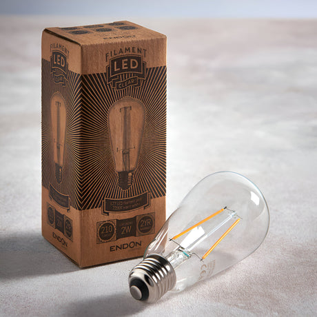 Endon 2W E27 LED filament pear bulb in clear glass with visible warm-tone filaments, lying beside its printed kraft retail box on a light surface.