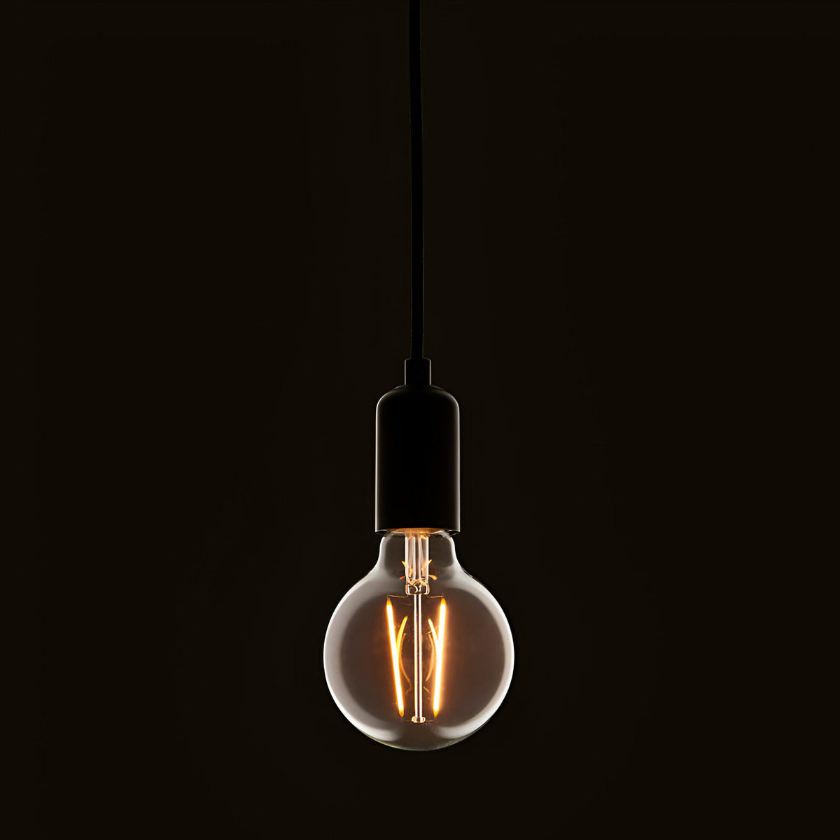 Pendant light fitted with a clear E27 LED filament globe bulb, glowing warm white against a dark background.