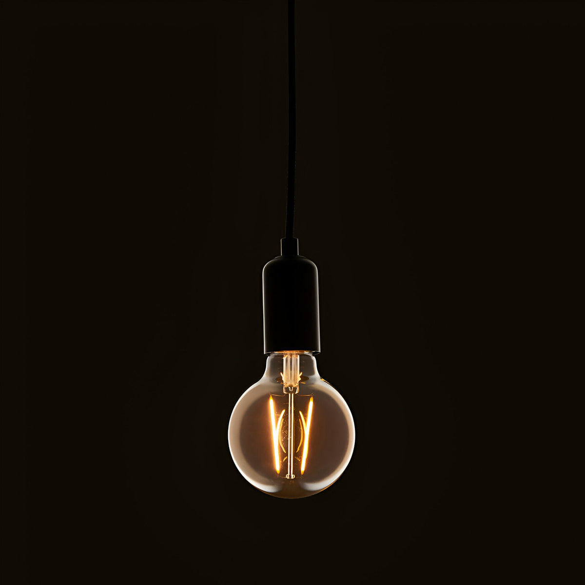 Pendant light fitted with a 2W E27 LED filament globe bulb in amber tinted glass, glowing warm white against a dark background.