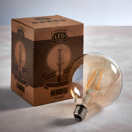 Endon 2W E27 LED filament globe bulb in amber tinted glass beside its printed brown cardboard box on a light neutral surface.
