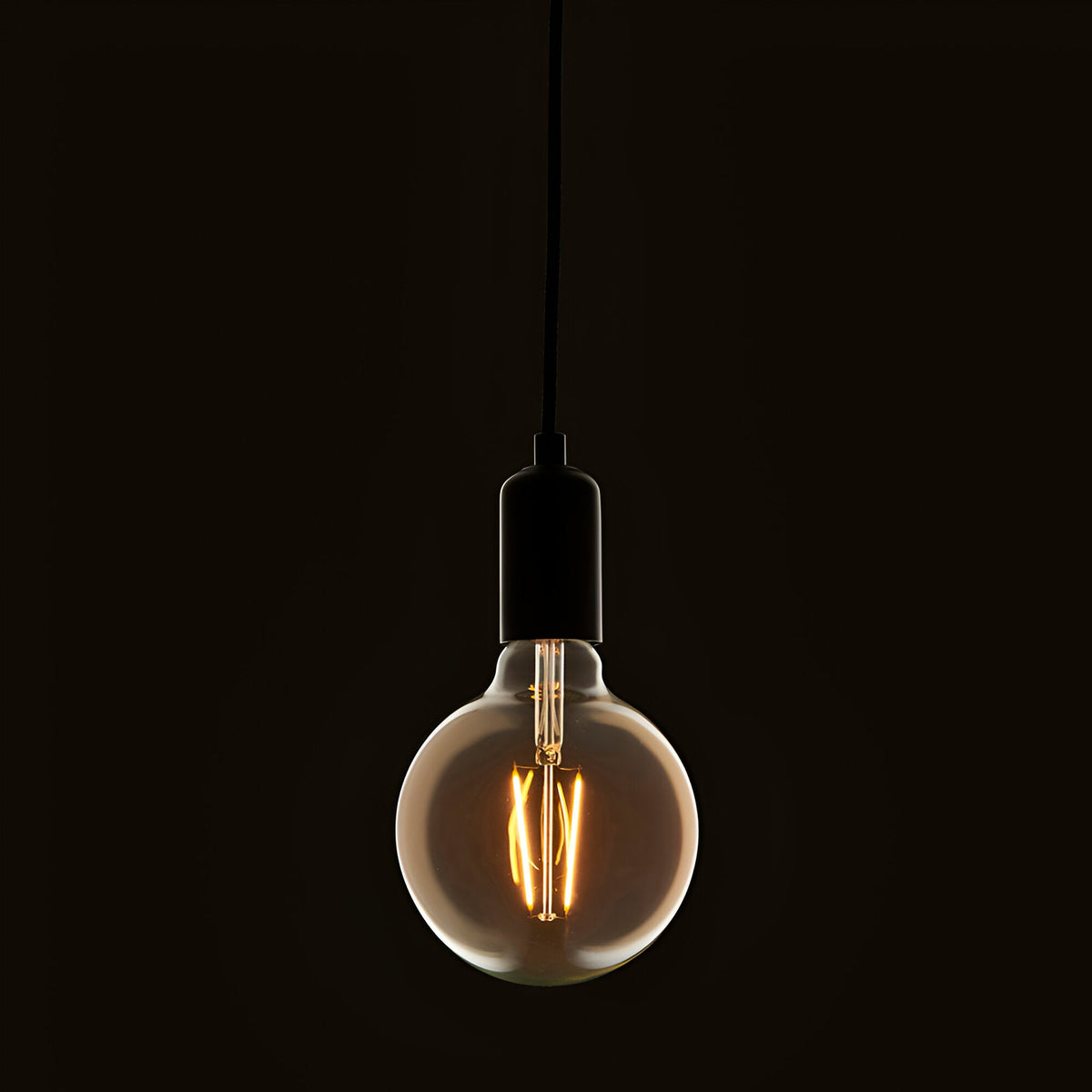 Endon 2W E27 LED filament globe bulb in amber tinted glass, suspended from a black pendant cord with matte black lampholder against a dark background.