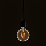 Endon 2W E27 LED filament globe bulb in amber tinted glass, suspended from a black pendant cord with matte black lampholder against a dark background.