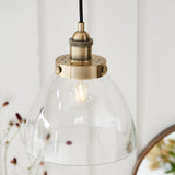 Endon Wentworth pendant light with clear glass dome shade and knurled antique brass lamp holder on black flex, hung in a light interior setting.