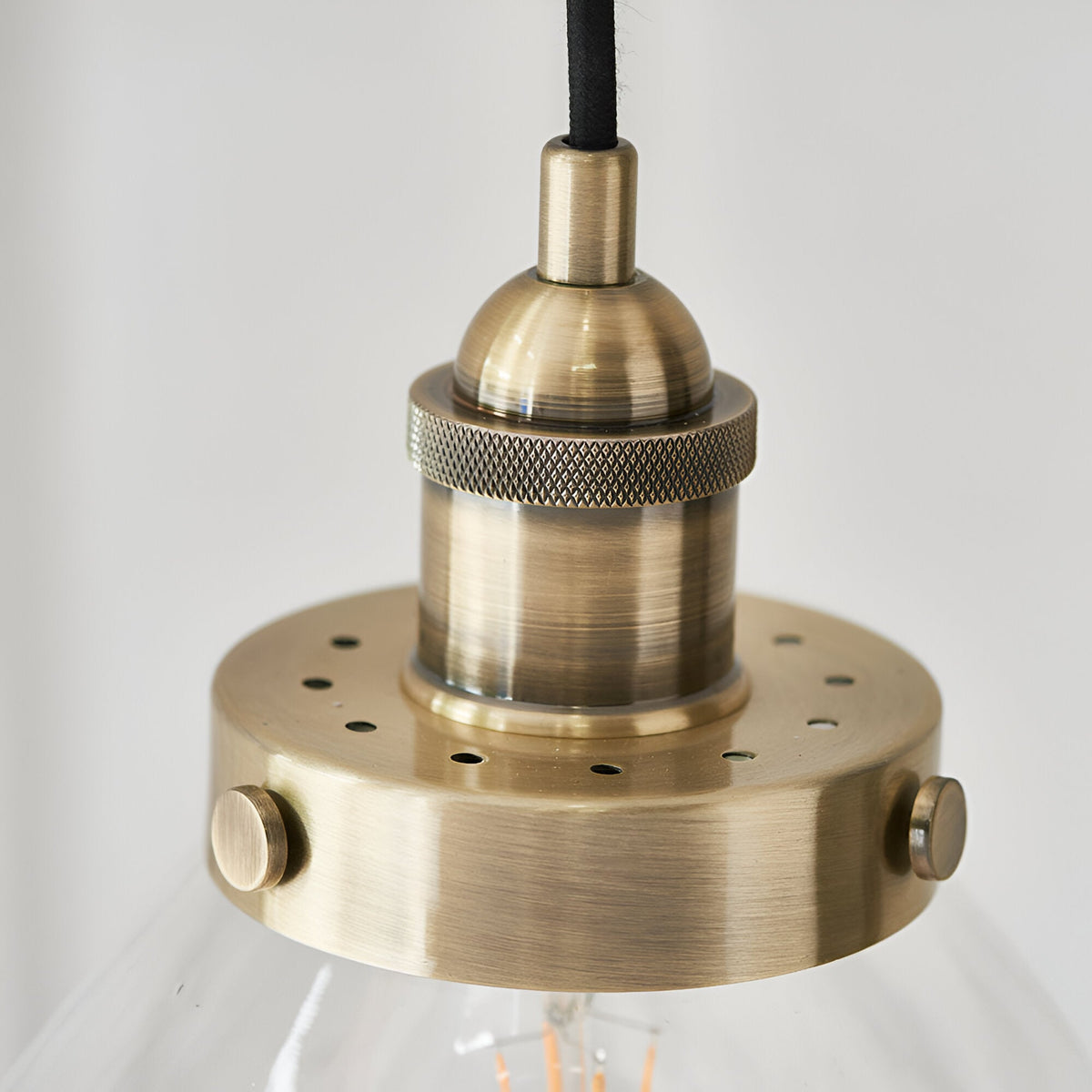 Close-up of Endon Wentworth Pendant Light in brass, showing the knurled E27 lamp holder, perforated disc and black fabric flex above a clear glass shade.